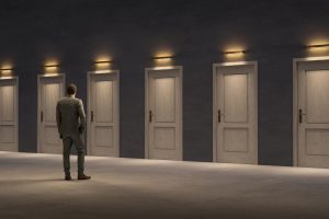 A man in a suit stands in front of several doors as he tries to decide which one to enter